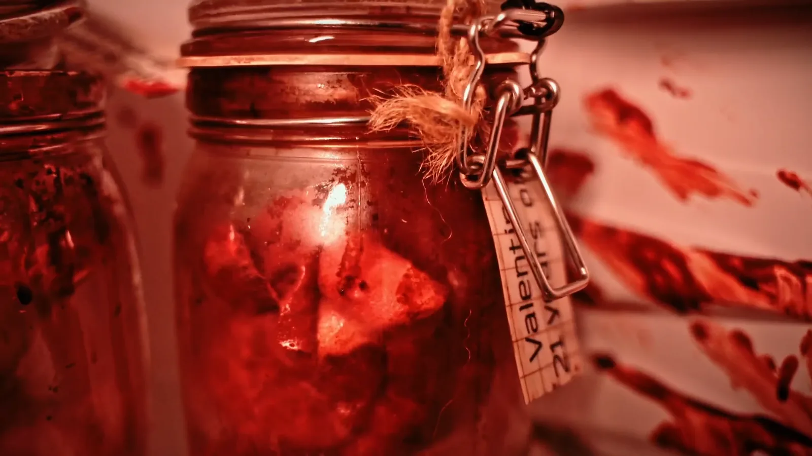 A grisly specimen jar with a handwritten tag, lit red, inside Buried Alive